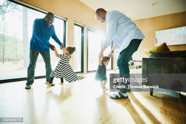 laughing grandfather and father dancing with granddaughter and daughter in living room - baby dancing stock-fotos und bilder