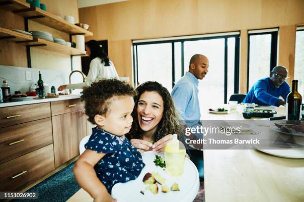 laughing mother helping toddler daughter with food during dinner with family - dedication background stock pictures, royalty-free photos & images