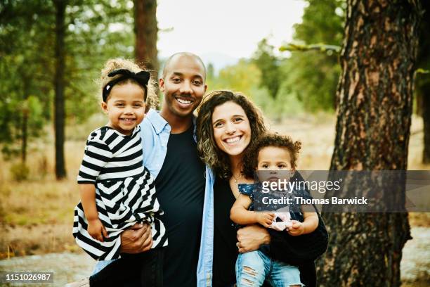 portrait of smiling parents holding two young daughters - mixed race family photos et images de collection