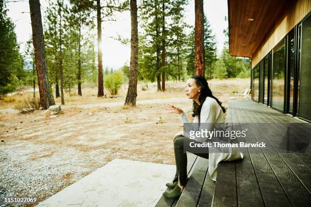 senior woman sitting on porch of cabin in woods - frank wood stock pictures, royalty-free photos & images