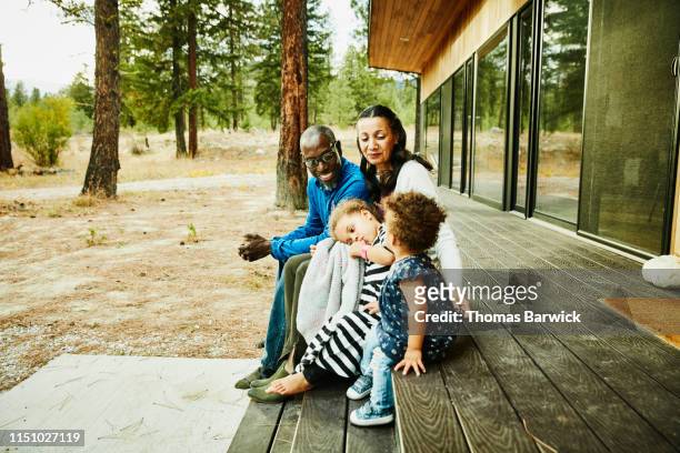 Smiling grandparents sitting with young granddaughters of porch of cabin