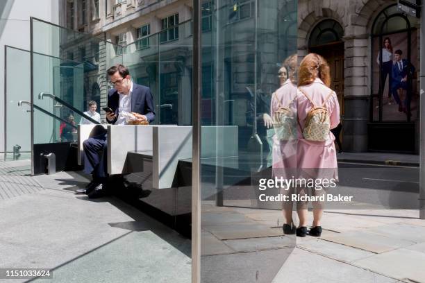 Ladies talk and a man uses his phone while sitting in sunshine during the lunchtime break on Threadneedle Street in the City of London, the capital's...