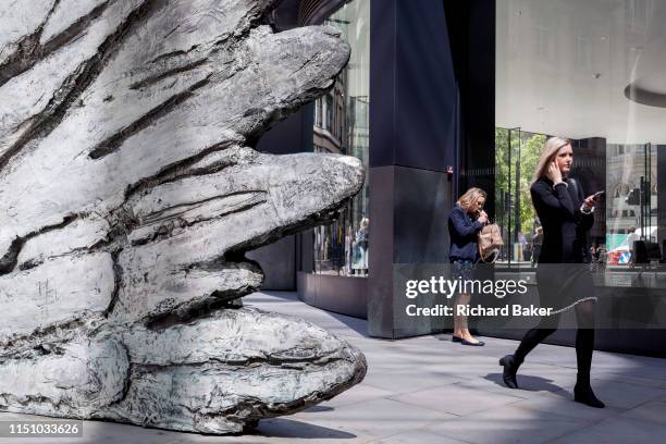 Lady lights a cigarette as a younger, healthier woman walks past the sculpture entitled 'City Wing' on Threadneedle Street in the City of London, the...