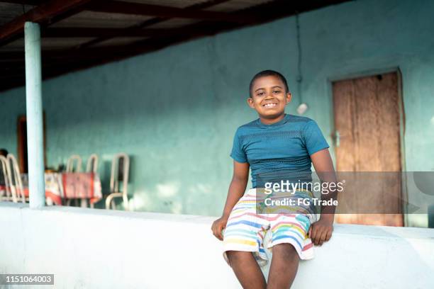 retrato de um menino ao ar livre em uma cena rural que senta-se em uma parede pequena - humility - fotografias e filmes do acervo