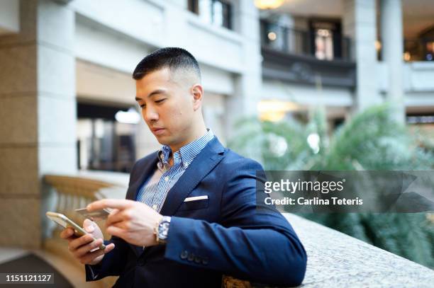 man making a mobile payment on his phone with credit card - wealthy asian man stock pictures, royalty-free photos & images