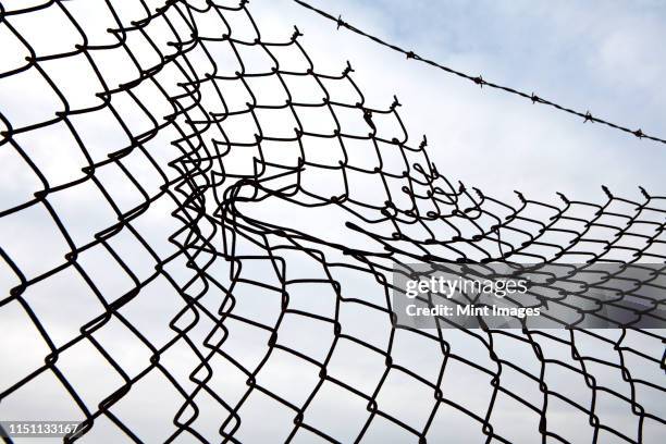 hole in chain link fence - chain fence stock-fotos und bilder