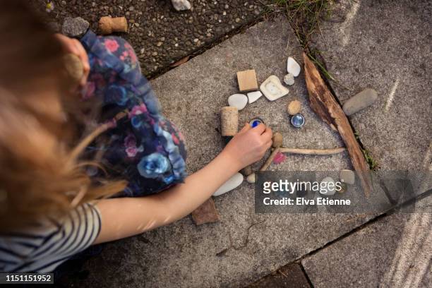 child creating anthropomorphic face shaped arrangement of a collection of discarded and natural objects found in an urban environment - holzstock stock-fotos und bilder