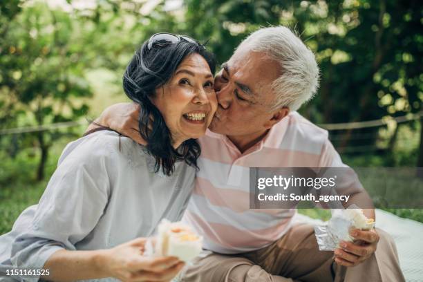 senior couple sharing love on picnic in park - asian wife stock pictures, royalty-free photos & images