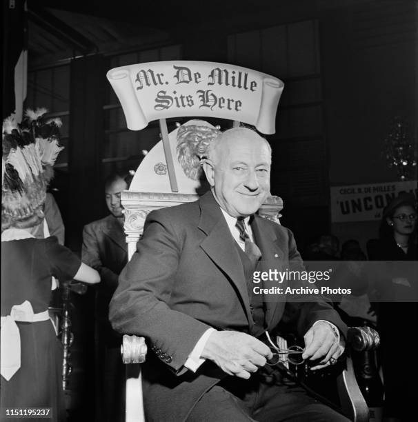 American filmmaker Cecil B DeMille seated on a chair with the sign 'Mr De Mille Sits Here' at an event marking the release of his film 'Unconquered',...
