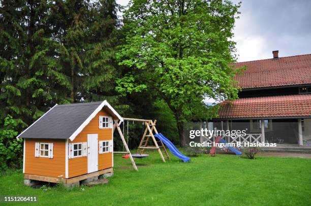 old traditional family home in spring,  with yellow playhouse and playground with swing and slides  in the back garden. grey weather. big green trees. - playhouse stock pictures, royalty-free photos & images