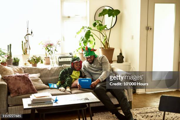 Father and son in dragon costumes using tablet on sofa