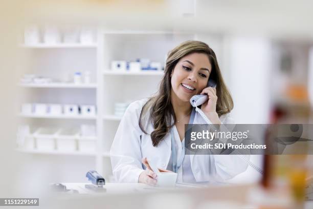 cheerful pharmacist consults with customer on telephone - pharmacist phone stock pictures, royalty-free photos & images