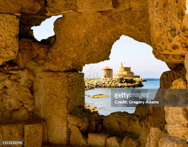 a view of the harbor entrance through a hole in a wall on rhodes, greece - rhodes,_new_south_wales stock pictures, royalty-free photos & images