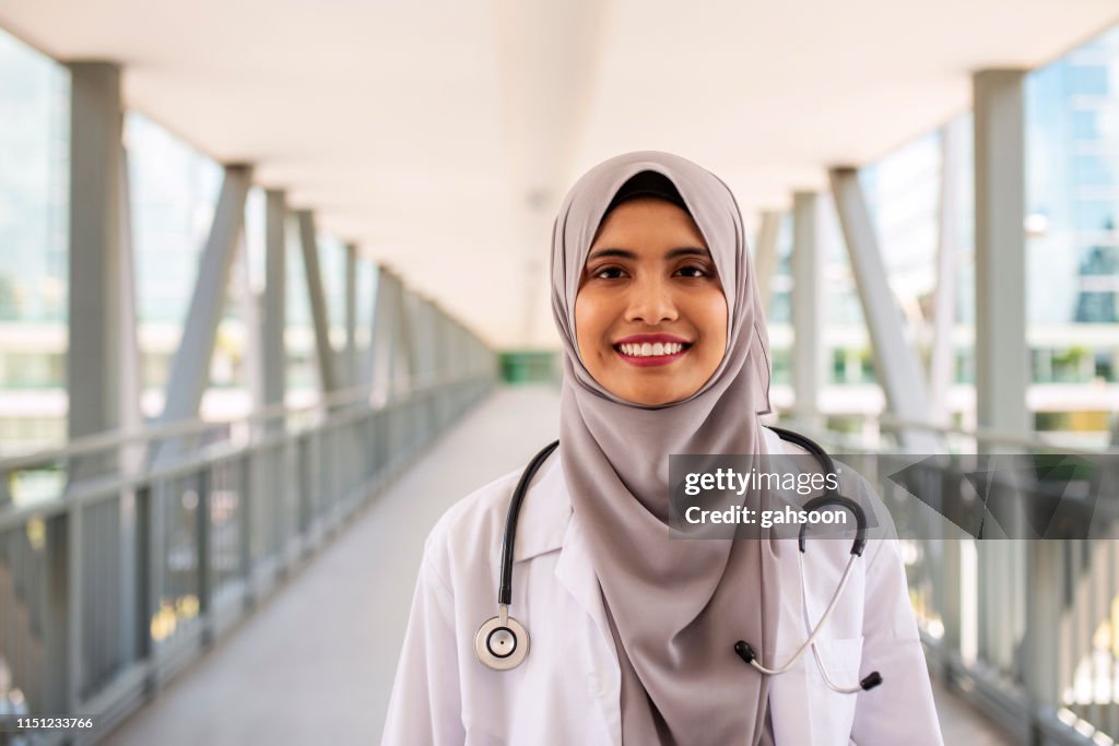 Portrait of confident Muslim doctor wearing hijab standing at the entrance of hospital