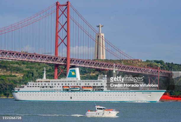 Deutschland, a cruise ship registered in Nassau, Bahamas, sails the Tagus River under the 25 de Abril Bridge while leaving harbor on her way to...