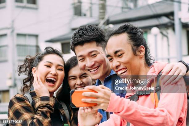 group of four cheerful friends looking at smartphone and laughing - hyper japan stock pictures, royalty-free photos & images