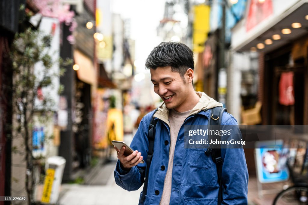 Fröhlicher junger Mann schaut sich Smartphone in der Straße an