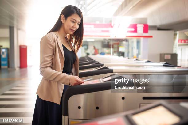 young asian woman wearing formal business suit paying the public transport fee by smart card at the subway gate - entering turnstile stock pictures, royalty-free photos & images