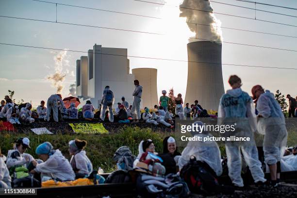 June 2019, North Rhine-Westphalia, Garzweiler: Activists stand and sit on the tracks of the coal transport railway in the evening and block it. The...