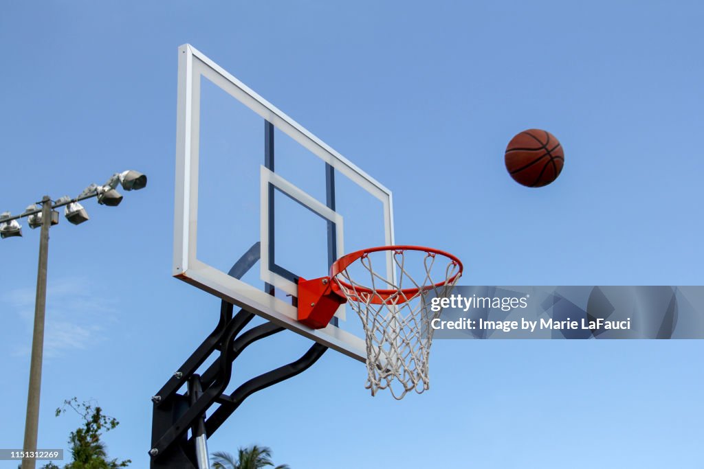 Basketball in midair near basketball hoop outdoors