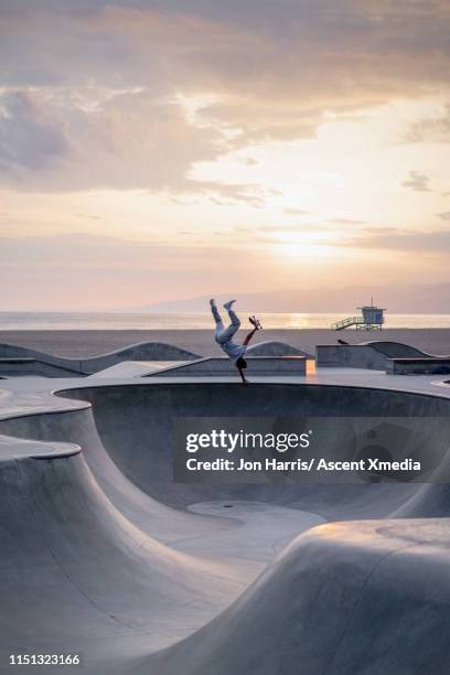 distant skateboarder performs stunts in park - venice beach photos et images de collection