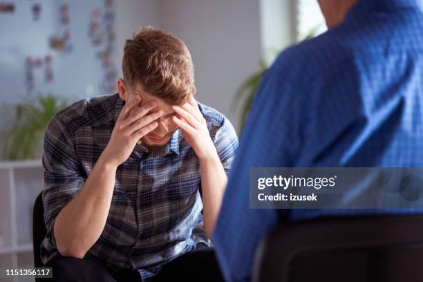 depressed male with head in hand during therapy - low self esteem stock pictures, royalty-free photos & images