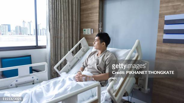 asian man look view out of window , the pain in the knee after surgery for fixing knee and for healing and recovery acl injuriesin on rehabilitation room in the hospital - beautiful asian legs stock-fotos und bilder