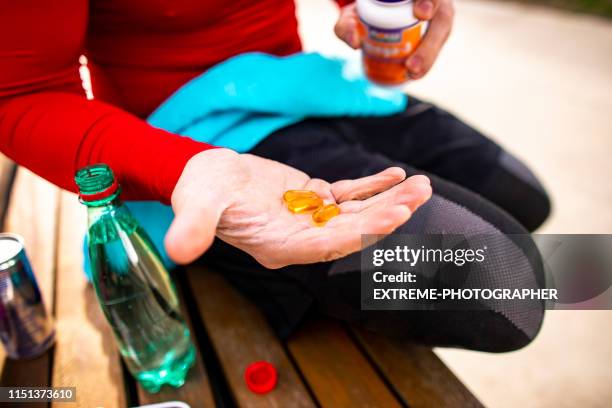 ein athletischer mann hält ein paar orange farbige kapseln auf der handfläche, während er auf einer parkbank sitzt - exercise pill stock-fotos und bilder