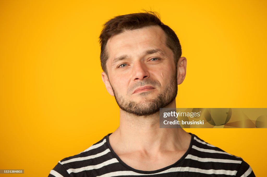 Studio portret van een 40 jaar oude bebaarde man in een gestreept t-shirt op een gele achtergrond