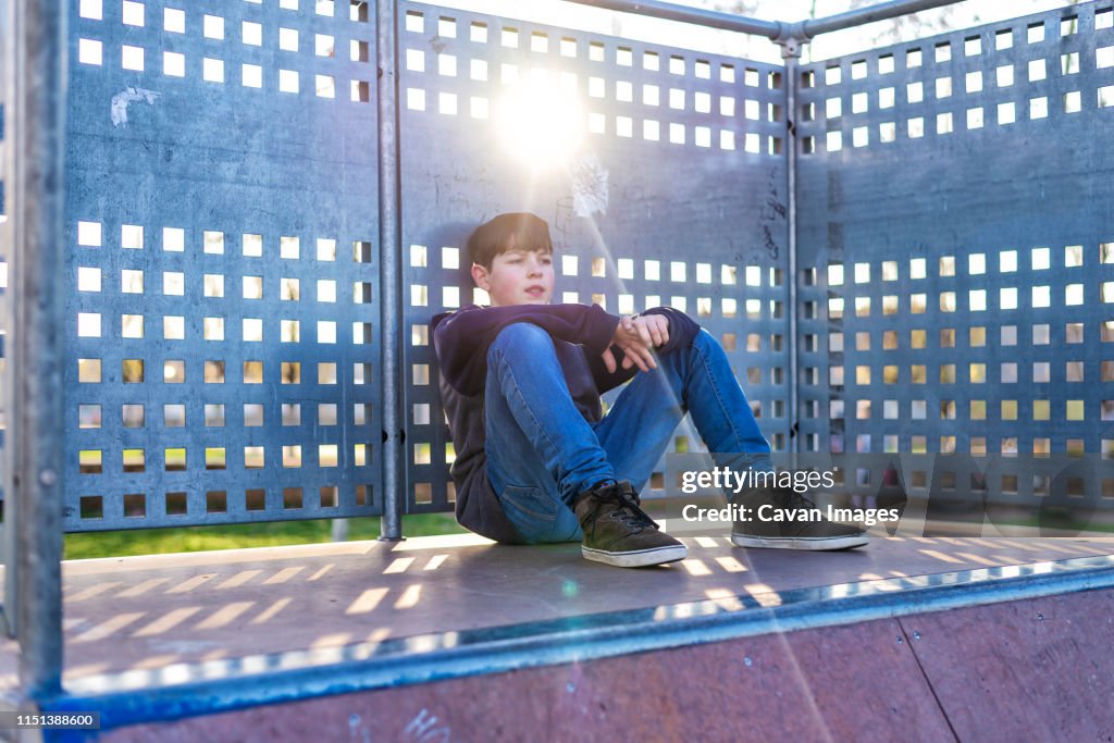 Portrait of young boy sitting looking away ,leaning on metallic fence
