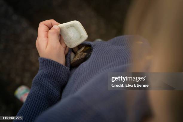 child holding small discarded piece of ceramic and with a pocketful of objects collected outdoors - stone hand stock-fotos und bilder