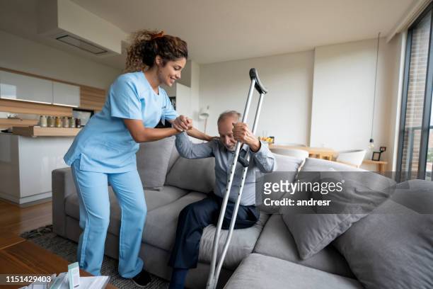 caregiver helping a senior man with a disability to stand up at home - amputee home stock pictures, royalty-free photos & images