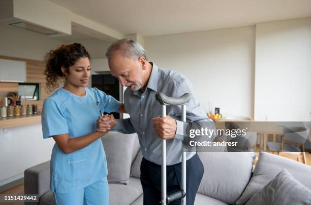 nurse helping a senior man in crutches at home - crutches stock pictures, royalty-free photos & images