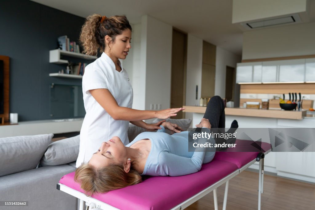 Masseuse helping a senior woman at home with her therapy exercises