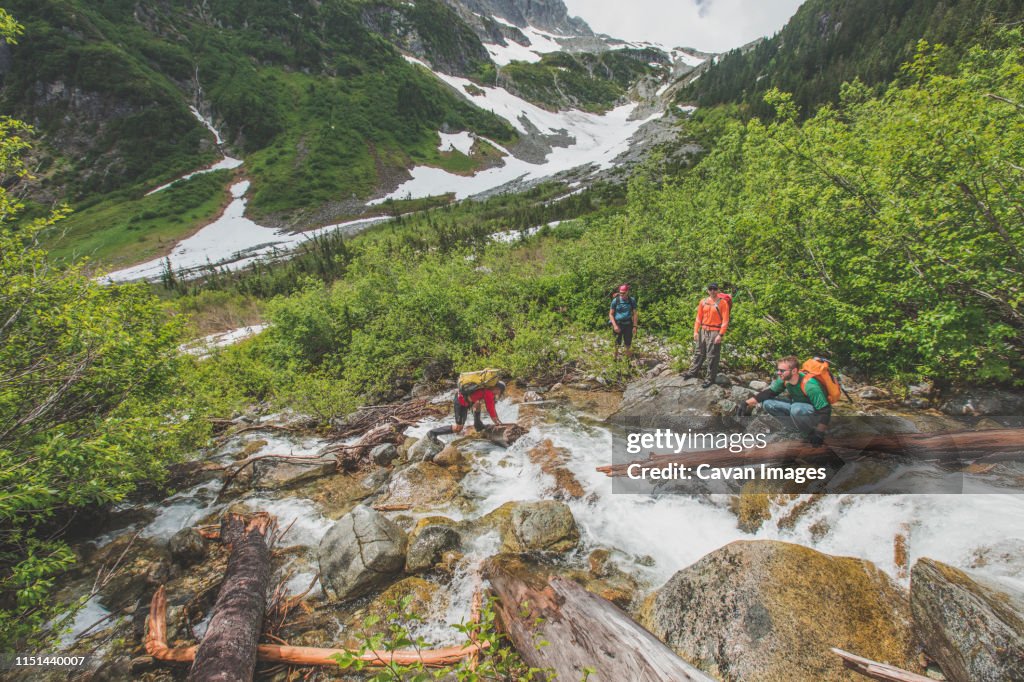 A group of backpackers carefully navigate across a raging river.