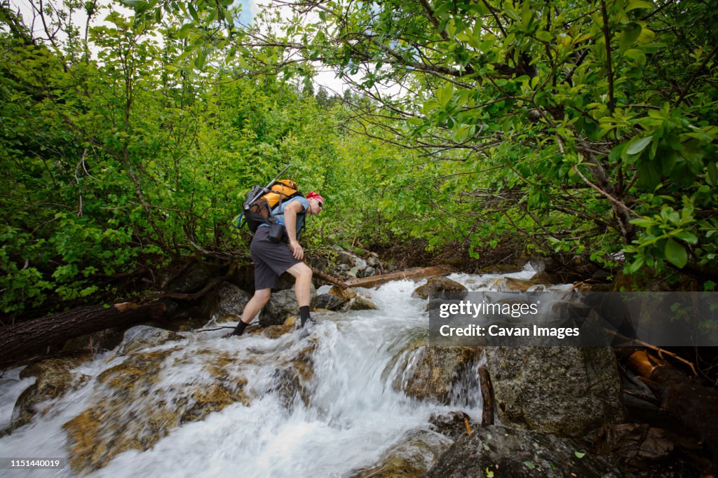 Backpacker carefully navigates across a raging river.