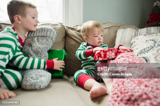 blonde toddler boy opens red gift with family on christmas morning - boy gift stock-fotos und bilder