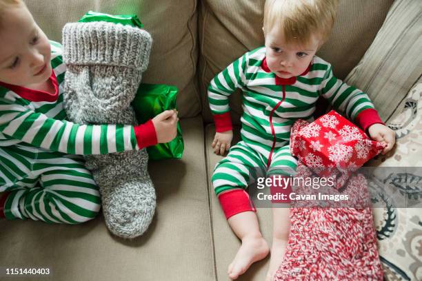 boy looks ahead while sitting next to brother with christmas stocking - kid stocking stock pictures, royalty-free photos & images