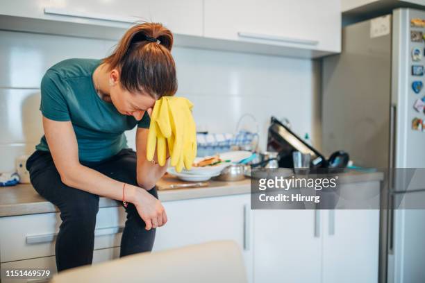 mulher que senta-se no contador da cozinha, prendendo luvas protetoras - homemaker - fotografias e filmes do acervo