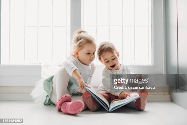 sisters reading a book together in a window seat - reading imagens e fotografias de stock