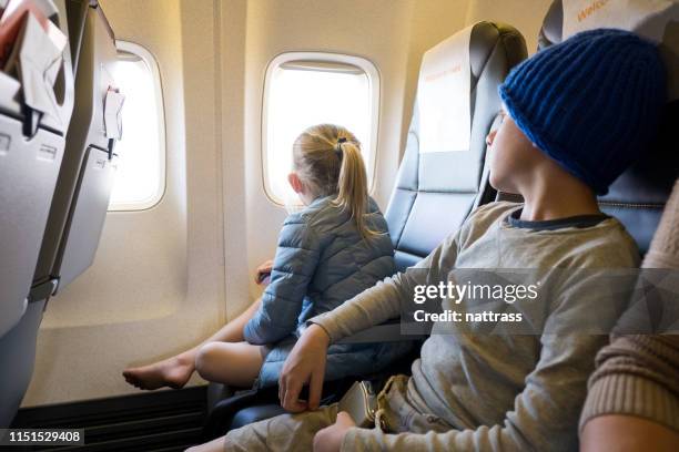 girl sitting by brother looking through window of airplane - middle stock pictures, royalty-free photos & images