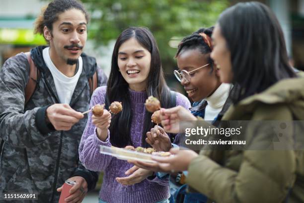 amigos felizes que comem o takoyaki do pacote na cidade - takoyaki - fotografias e filmes do acervo