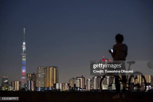 Man uses a smartphone in front of the Tokyo Skytree illuminated with the colors of the U.S. National flag at night on May 25, 2019 in Tokyo, Japan....