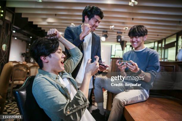 junge freunde spielen handyspiel im café - cell mates stock-fotos und bilder