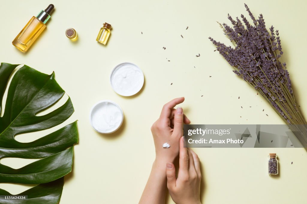Top view and flat lay of woman holding cream on hands over white table with cosmetic products - avocado oil, cream and bamboo