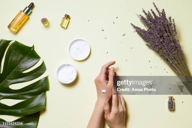 top view and flat lay of woman holding cream on hands over white table with cosmetic products - avocado oil, cream and bamboo - cream coloured imagens e fotografias de stock