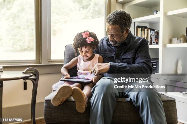 granddaughter showing grandfather how to use tablet - wealthy family inside home stock pictures, royalty-free photos & images
