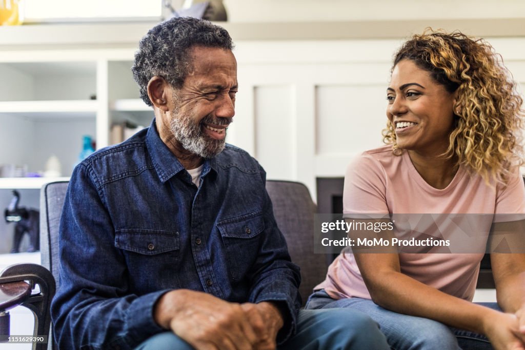 Senior man and adult daughter talking on couch