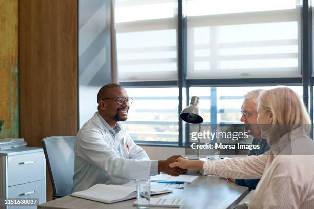 smiling doctor shaking hand with senior woman - couple shaking hands with doctor stock pictures, royalty-free photos & images