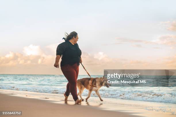 mujer caminando al atardecer con su perro husky siberiano en la playa - complexión gruesa fotografías e imágenes de stock